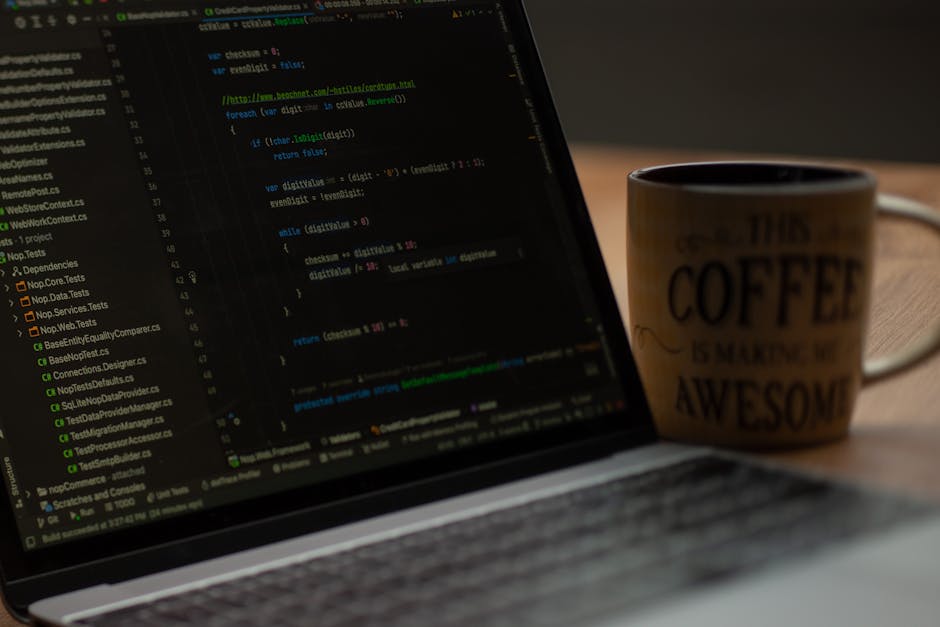 A close-up photograph of a computer screen displaying lines of code with syntax highlighting in various colours such as green, blue, purple, and white on a dark background. To the left, a directory st